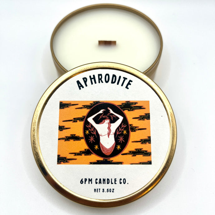 A travel-sized candle with Aphrodite fragrance, made by 6pm Candle Co., in a tin with a lid featuring an illustration of a woman