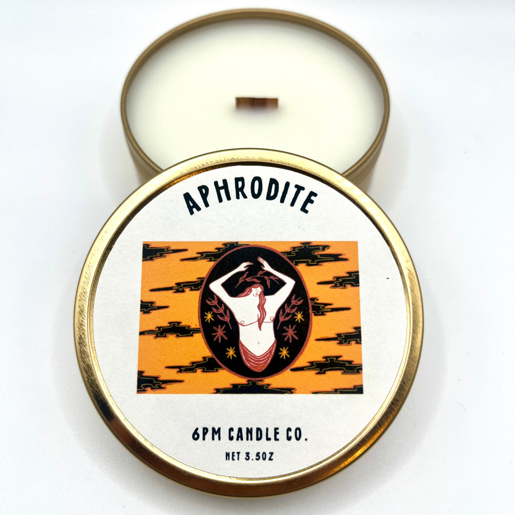 A travel-sized candle with Aphrodite fragrance, made by 6pm Candle Co., in a tin with a lid featuring an illustration of a woman