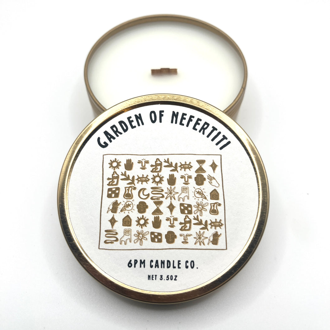 A travel-sized soy wax candle with a wooden wick, labeled 'GARDEN OF NEFERTITI' along with the brand '6pm Candle Co.'