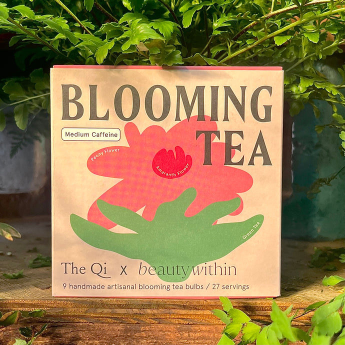 A package of 'Blooming Tea' by The Qi, featuring a floral design and a clear window showing handmade artisanal bloom tea bulbs.